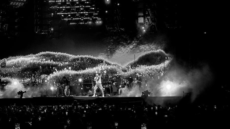 Post Malone performing with his live band, featuring a sunflower hill backdrop.